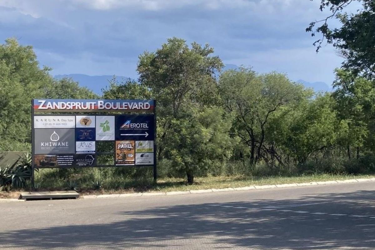 A street-level view of a commercial signage board located at the entrance of Zandspruit Boulevard, featuring various local business advertisements.