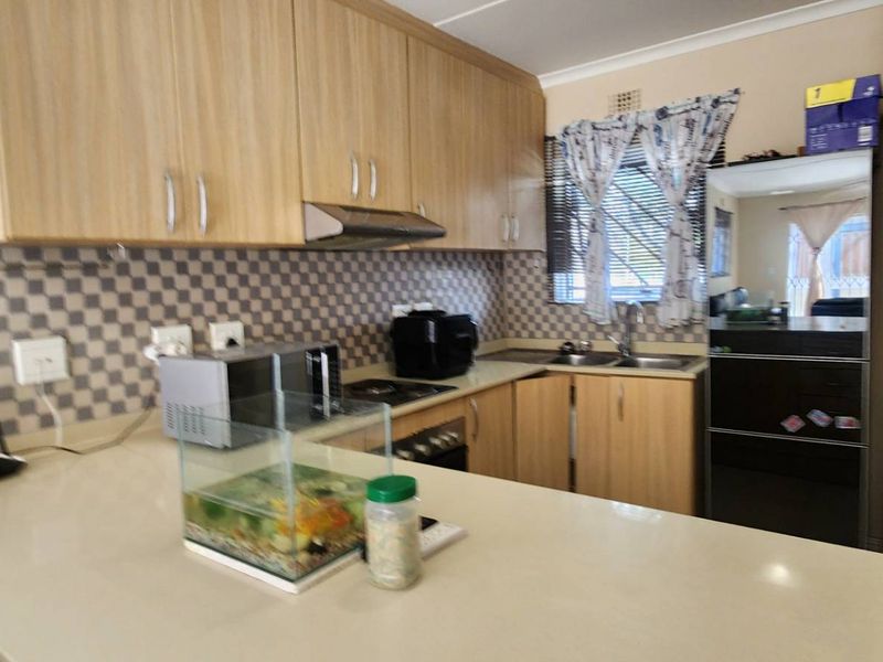 Functional kitchen featuring light wood-finish cabinetry, stone countertops, a tiled backsplash, and integrated cooking appliances.
