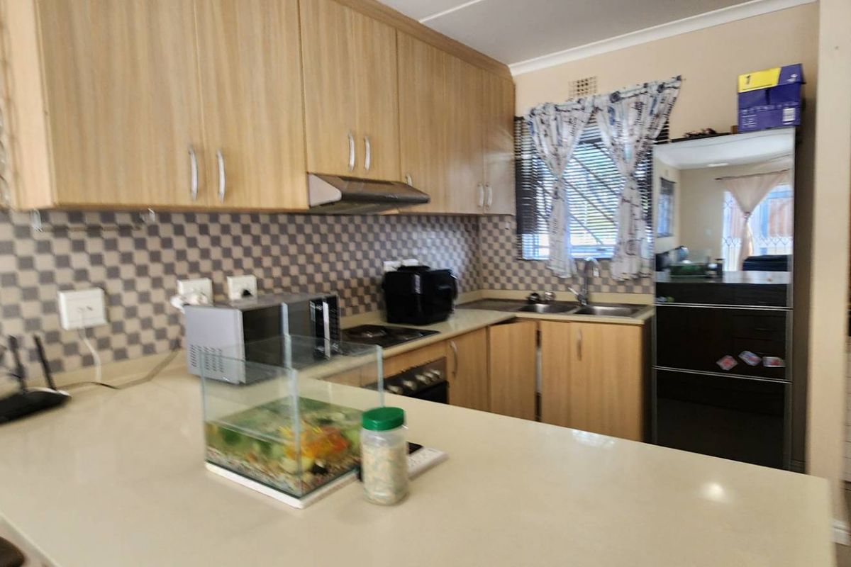 Functional kitchen featuring light wood-finish cabinetry, stone countertops, a tiled backsplash, and integrated cooking appliances.