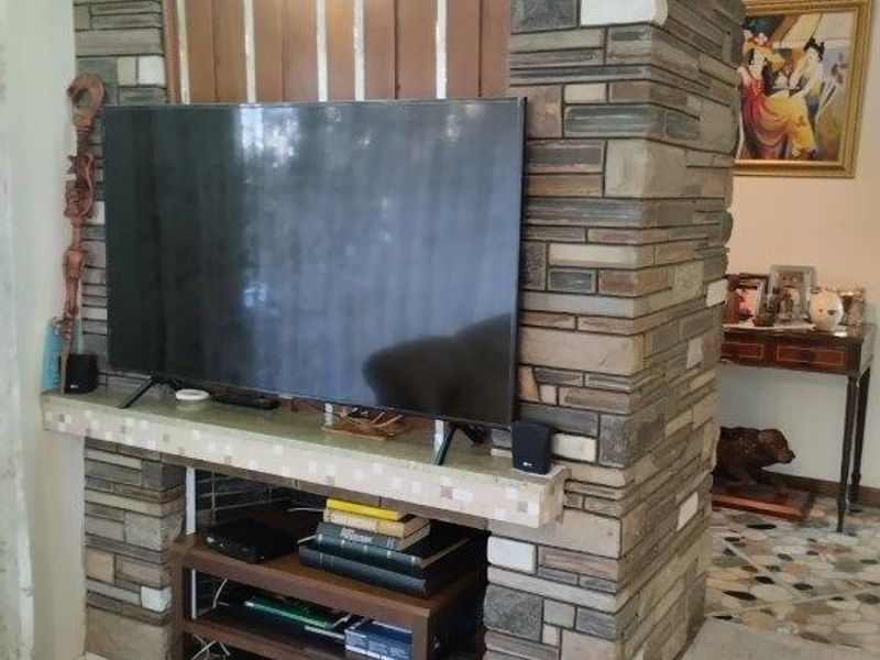 A living room featuring a prominent stone-clad feature wall with a built-in shelf and integrated lighting, leading to a raised tiled area.