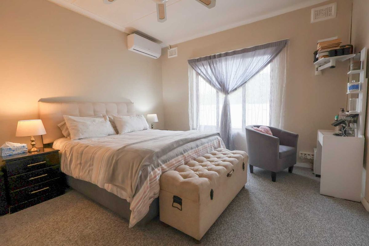 A well-lit bedroom featuring a wall-mounted air conditioning unit, carpeted flooring, and a ceiling fan.