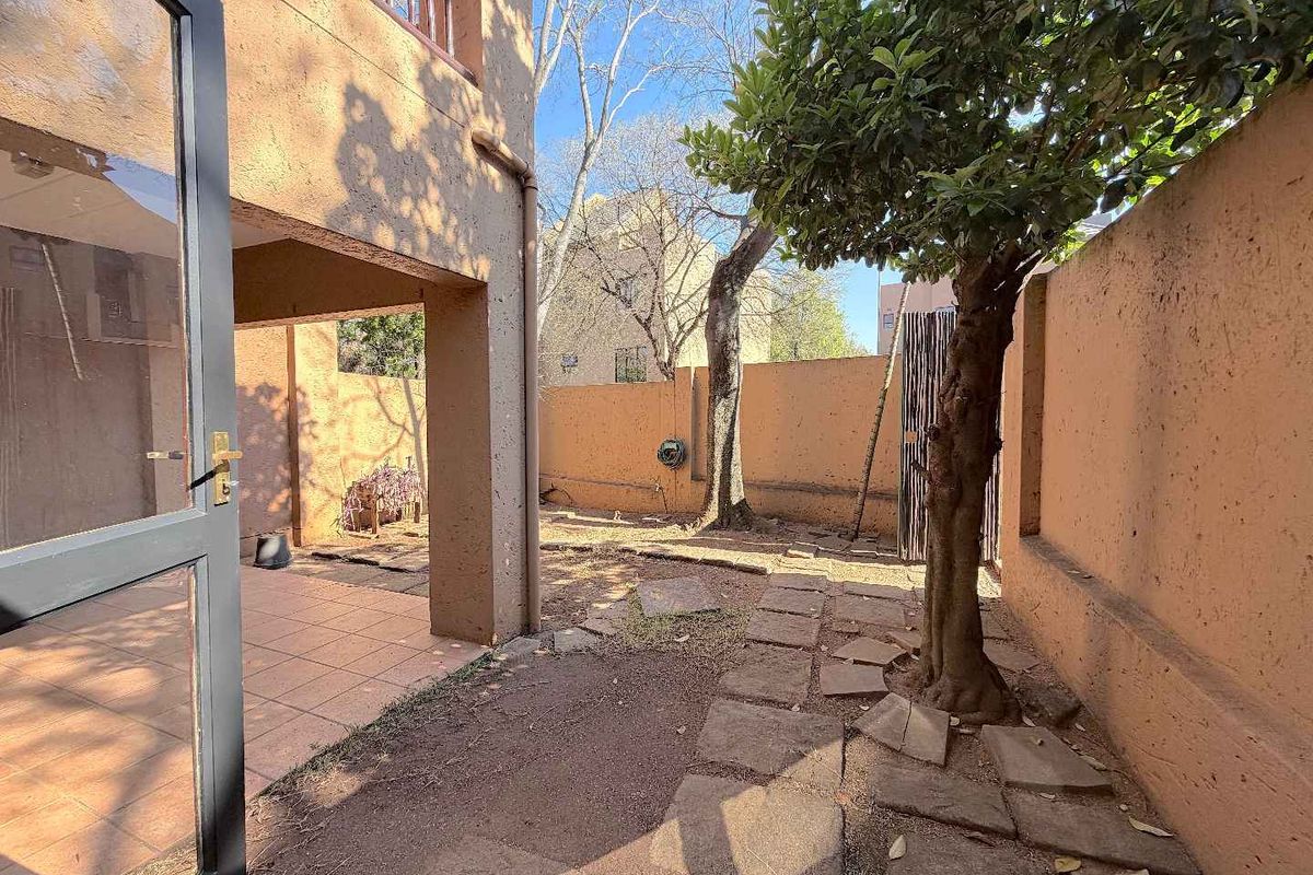 A private rear courtyard featuring a tiled patio area, paved garden path, and high boundary walls, offering a quiet outdoor space.