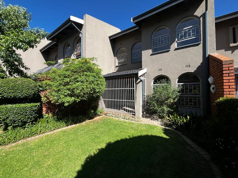Rear view of the townhouse featuring a private garden, paved walkway, and arched windows with security bars.