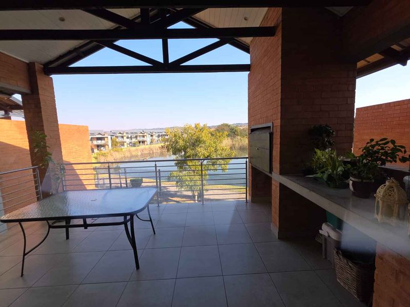 Spacious covered balcony featuring a built-in braai, concrete prep surface, and exposed brickwork, offering scenic views over the estate lake.
