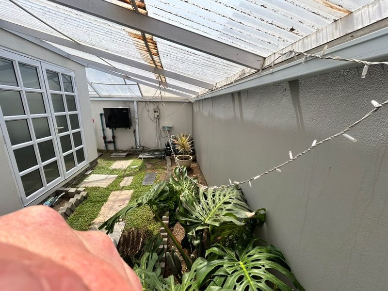 A covered outdoor patio area featuring a corrugated roof structure, paved walkway, and direct access to the home via french doors.