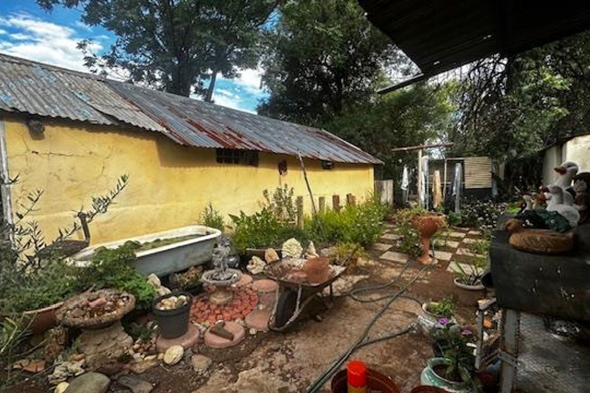Rear exterior view of the property featuring a corrugated metal roof, weathered yellow plaster walls, and a garden area with paved sections.