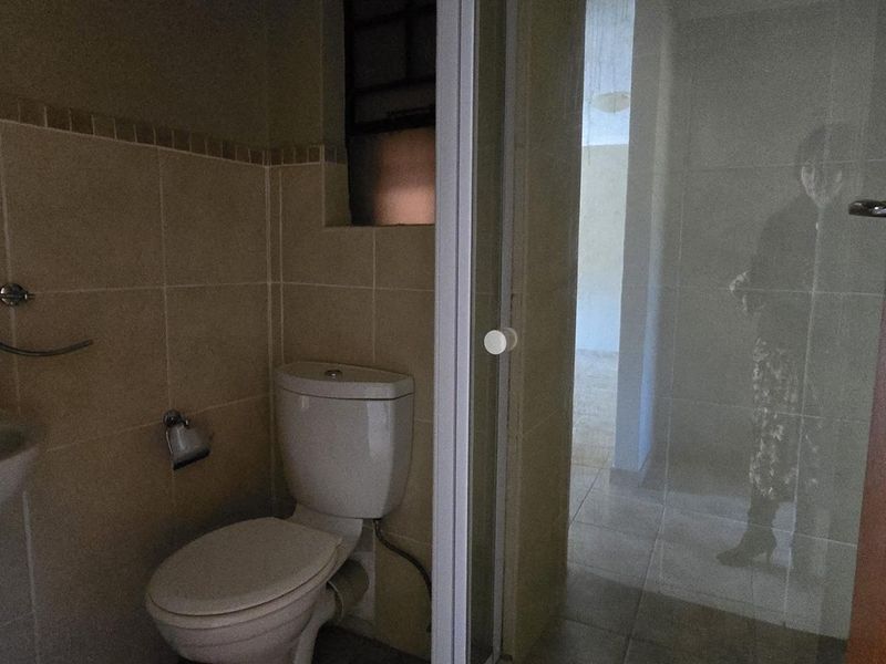 A functional bathroom featuring a pedestal basin, toilet, and a glass-enclosed shower with neutral wall and floor tiling.