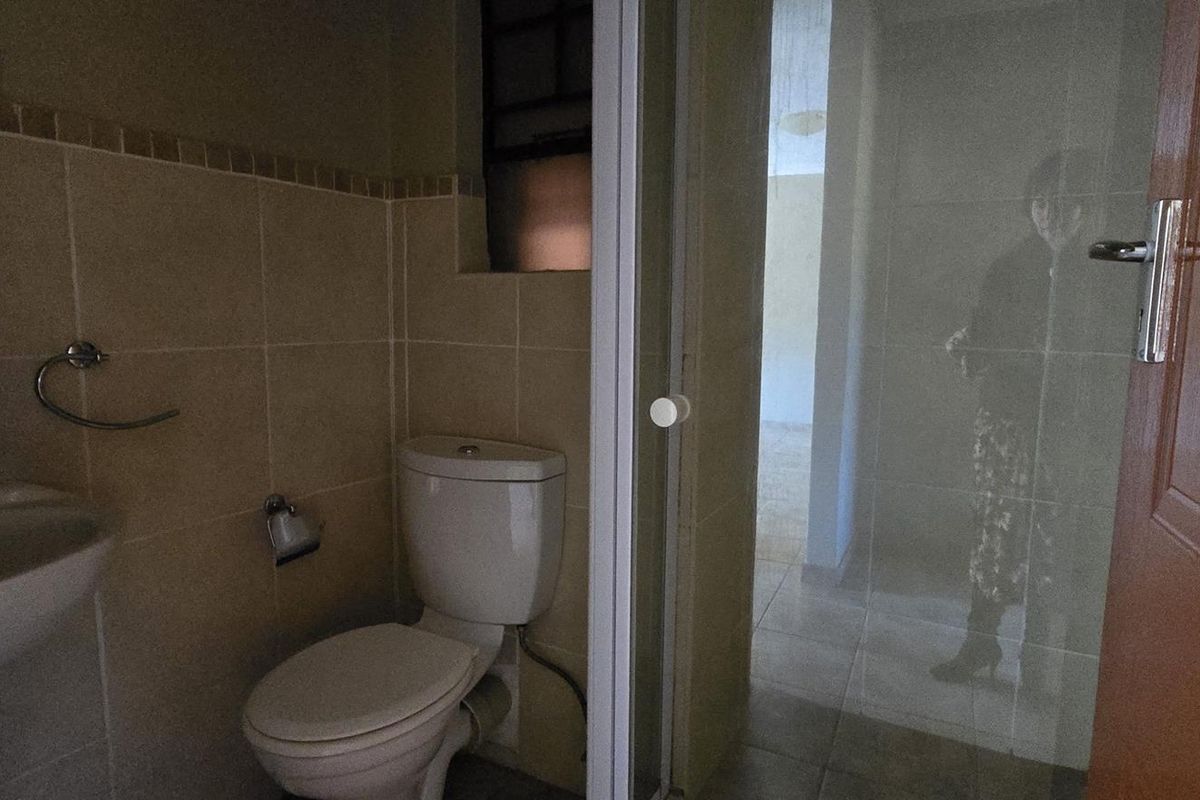 A functional bathroom featuring a pedestal basin, toilet, and a glass-enclosed shower with neutral wall and floor tiling.