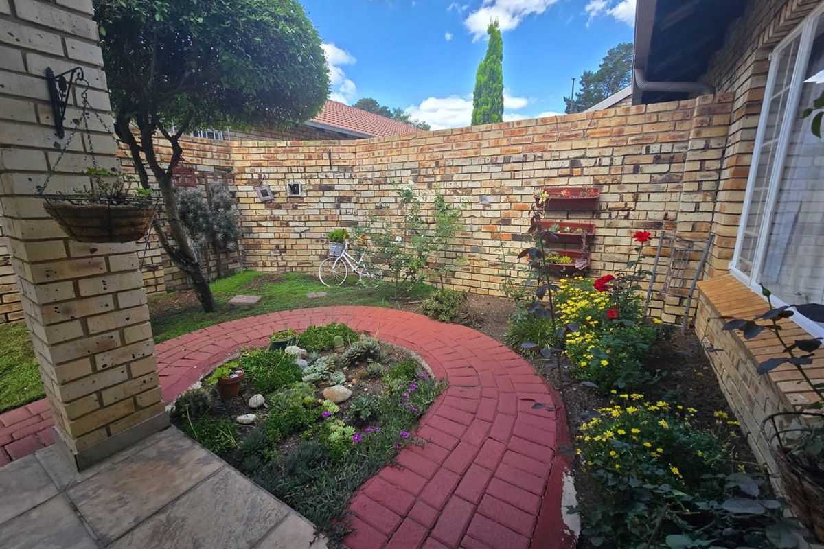 A private rear courtyard featuring a face brick boundary wall, a paved circular walkway, and a well-maintained garden bed adjacent to a tiled patio.
