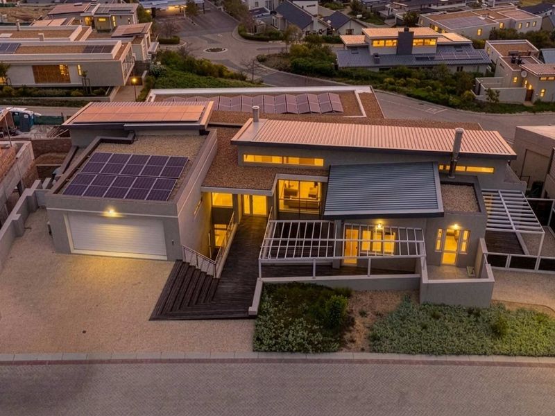 Aerial view of a modern residential property featuring solar panels, a metal roof, timber decking, and a paved driveway in a suburban estate.