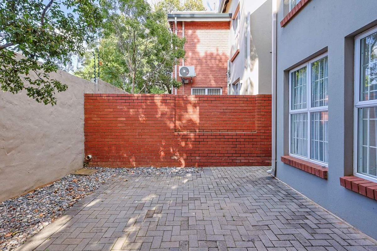 A private paved courtyard area featuring a brick boundary wall and gravel landscaping, adjacent to the townhouse exterior.