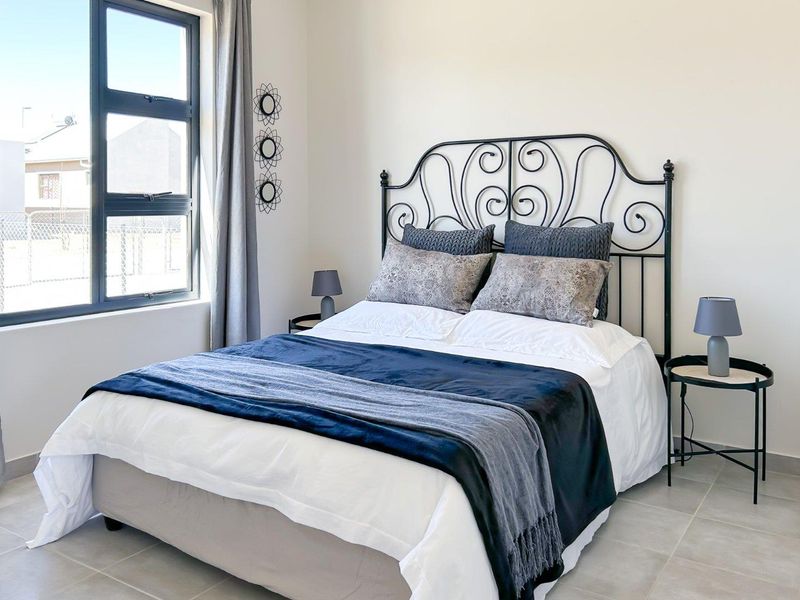 A well-lit bedroom featuring neutral walls, tiled flooring, and a large aluminium-framed window providing natural light.