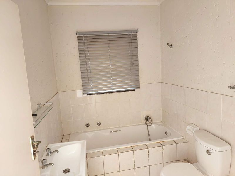 A compact bathroom featuring a standard bathtub, toilet, and washbasin with tiled walls and window blinds, requiring some maintenance and cosmetic updates.