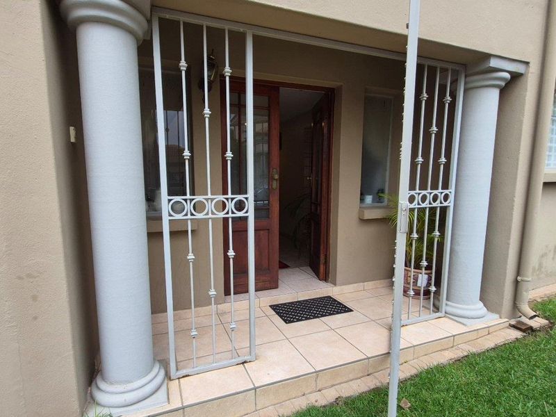 Front entrance featuring a tiled porch, decorative columns, and a secure metal gate leading to a timber front door.