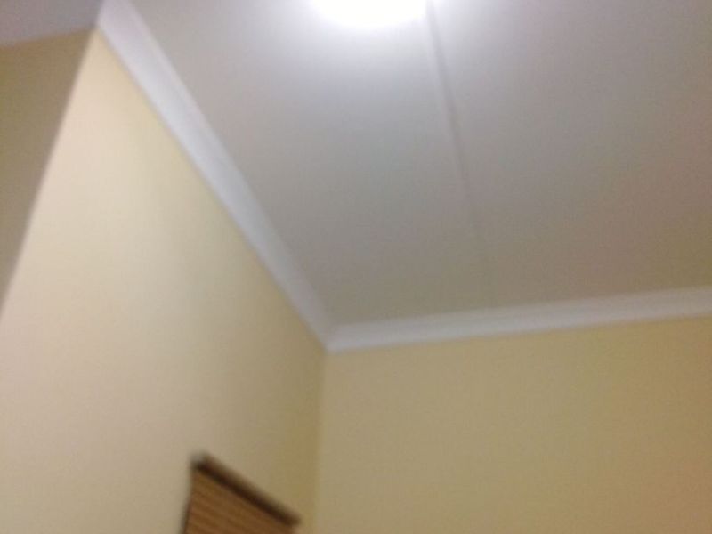 A view of a corner of a room featuring ceiling cornicing and a window blind.
