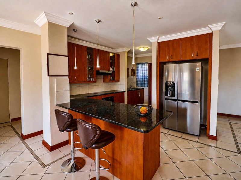 A well-maintained kitchen featuring wooden cabinetry, granite countertops, a breakfast bar, and tiled flooring, offering a functional and classic layout.