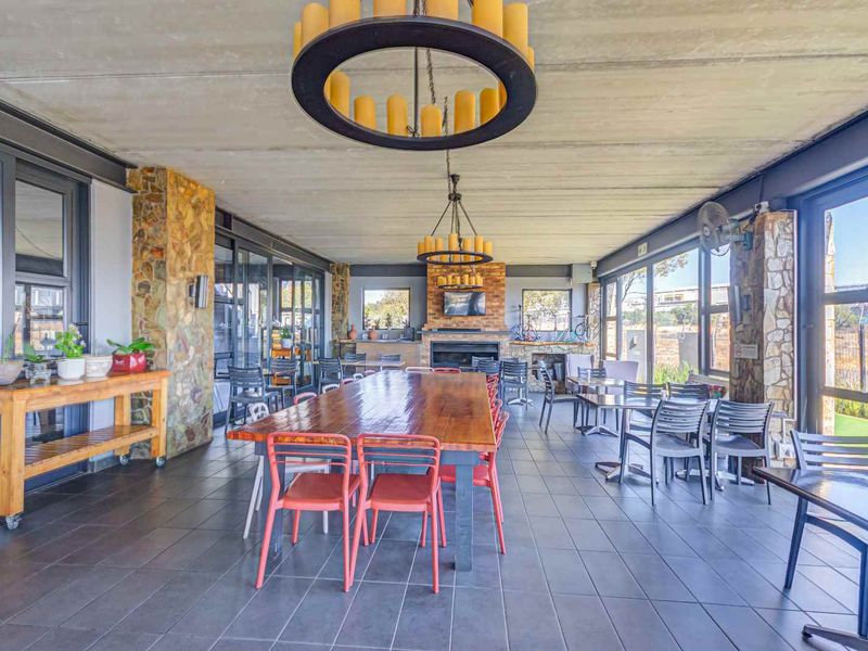 Spacious covered patio featuring stone-clad pillars, a built-in fireplace, tiled flooring, and large sliding glass doors, ideal for outdoor dining and entertainment.
