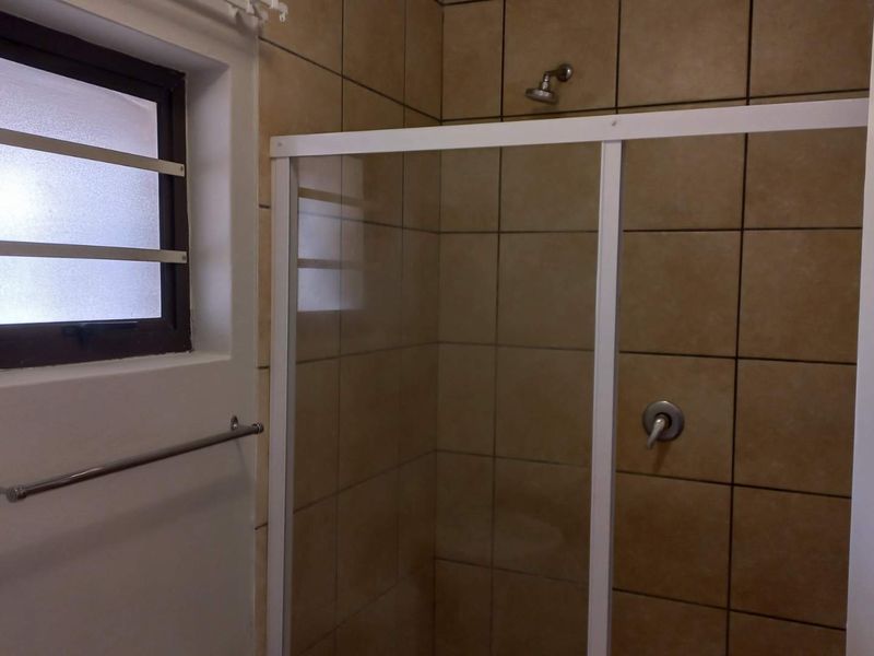 A functional bathroom shower area featuring tiled walls, a sliding glass shower enclosure, and a frosted window with security bars.