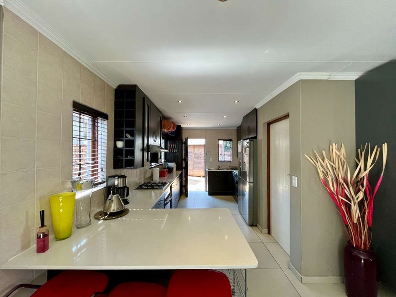 Modern kitchen featuring dark cabinetry, stone countertops, gas hob, and integrated appliances, leading through to a secondary scullery area with tiled flooring throughout.