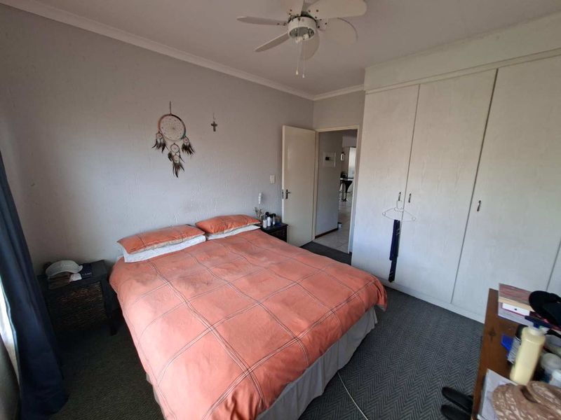 A functional bedroom featuring built-in cupboards and a ceiling fan, offering a practical layout with direct access to the hallway.