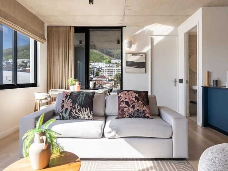 Modern open-plan living area featuring an exposed concrete ceiling, light wood flooring, and seamless access to a balcony with scenic views.