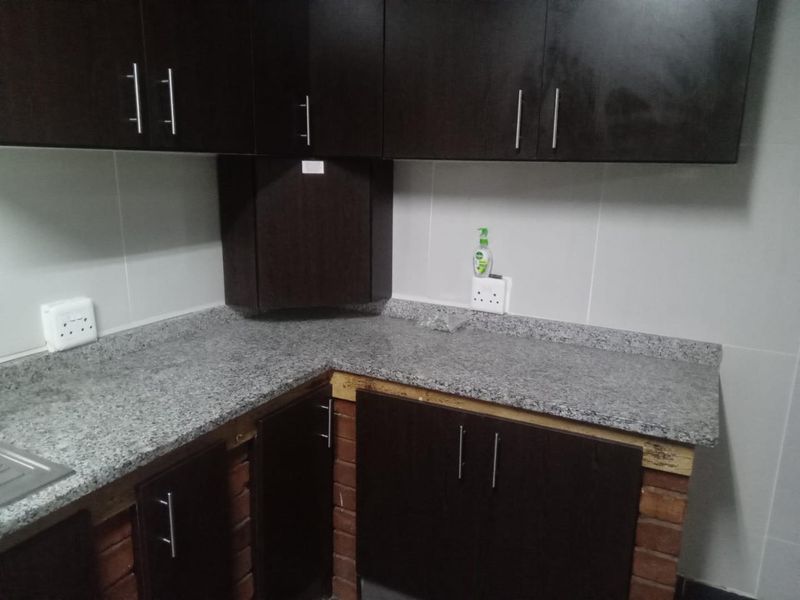 A functional kitchen area featuring dark wood cabinetry, granite countertops, and an exposed brick base, providing a solid foundation for further aesthetic updates.