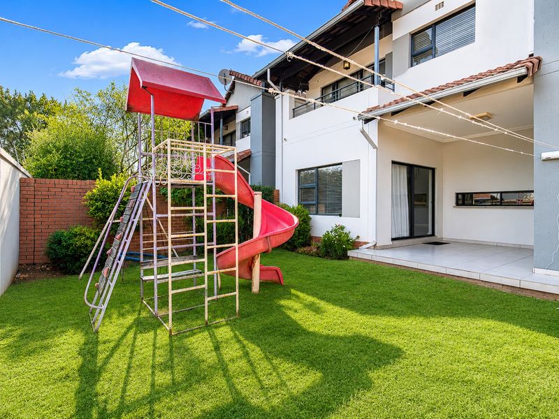Rear view of the townhouse featuring a covered tiled patio, manicured lawn, and brick boundary wall, providing a private outdoor space.