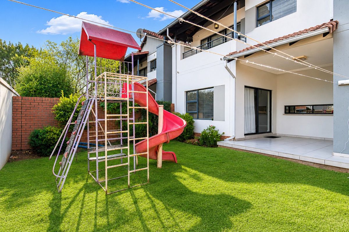 Rear view of the townhouse featuring a covered tiled patio, manicured lawn, and brick boundary wall, providing a private outdoor space.