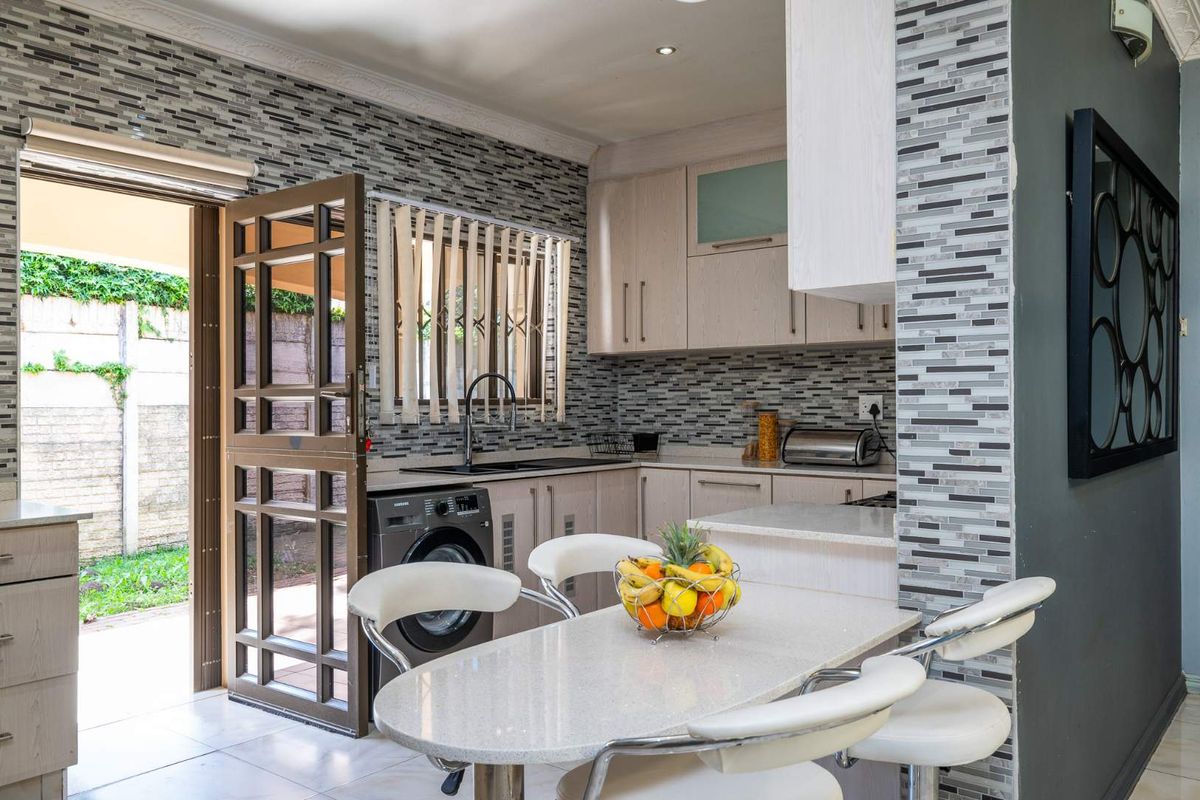 Modern kitchen featuring light-toned cabinetry, stone-look countertops, mosaic tile backsplash, and an integrated laundry area with direct access to the rear patio.
