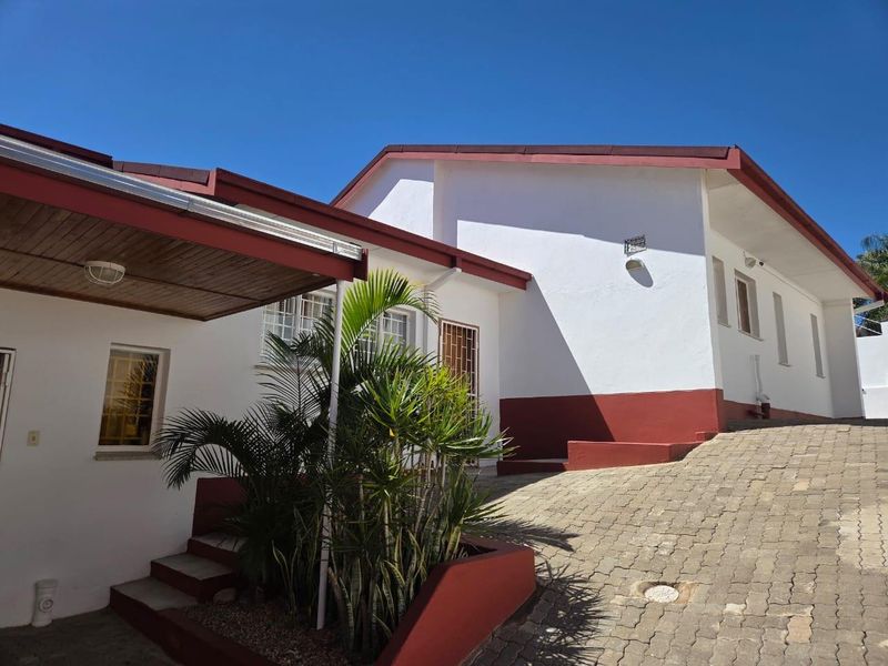 A well-maintained rear exterior view featuring a paved driveway, covered patio area, and clean white facade with contrasting trim.