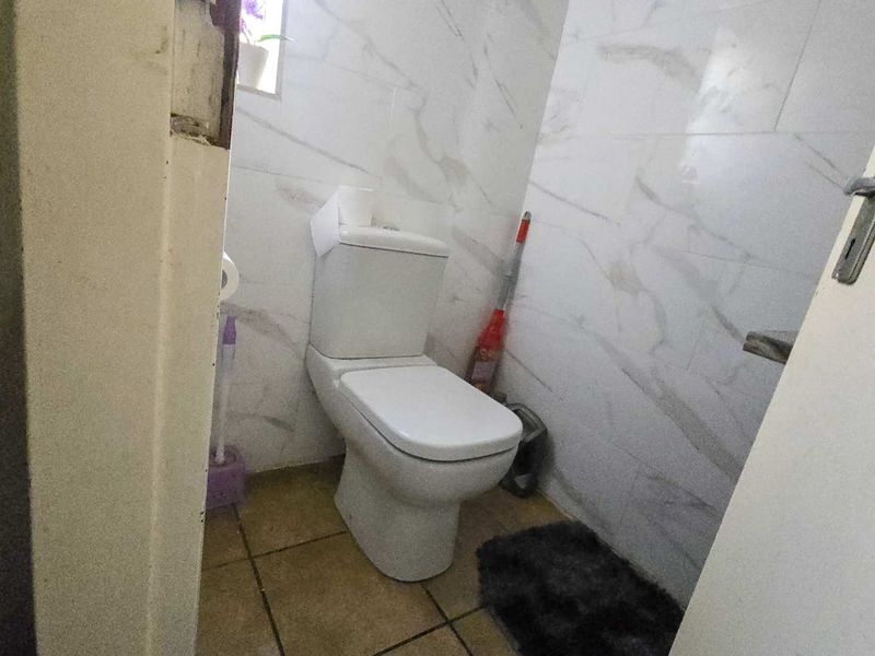 A small bathroom featuring marble-look wall tiles and a standard toilet, currently showing signs of wear around the door frame.