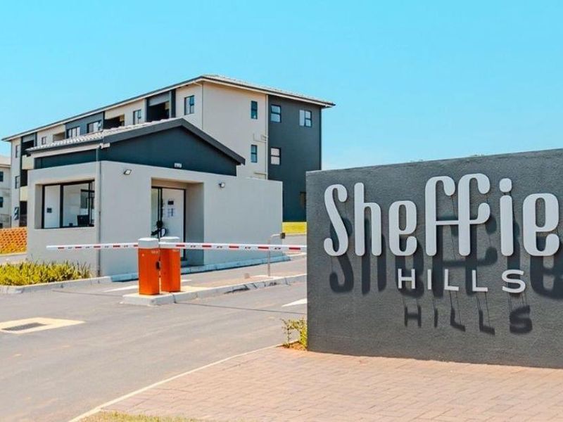 The entrance to Sheffield Hills apartment complex, featuring a secure boom gate, guard house, and modern multi-story residential buildings.