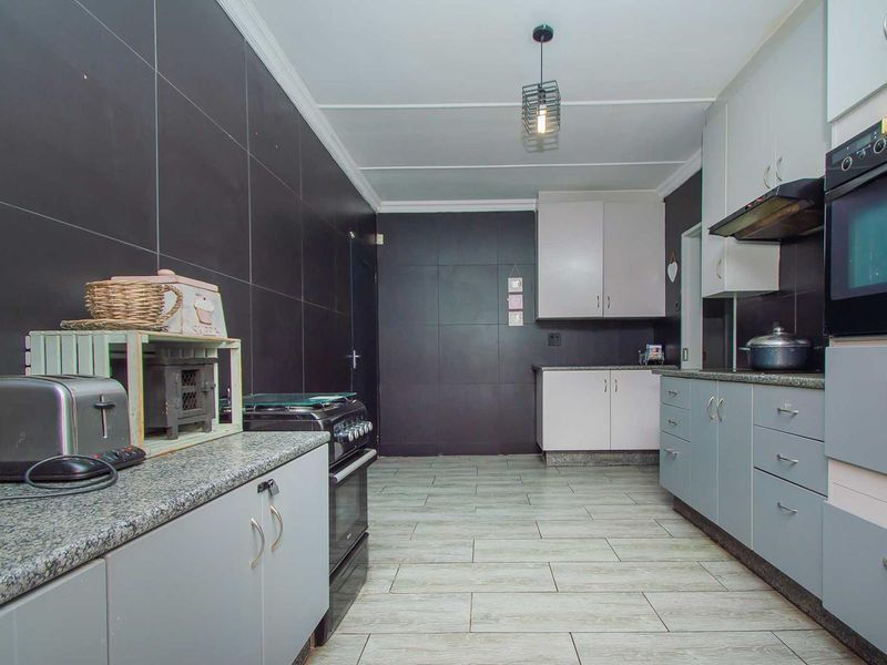 A functional kitchen featuring granite countertops, built-in cabinetry, a built-in oven with extractor fan, and modern tiled flooring and wall finishes.