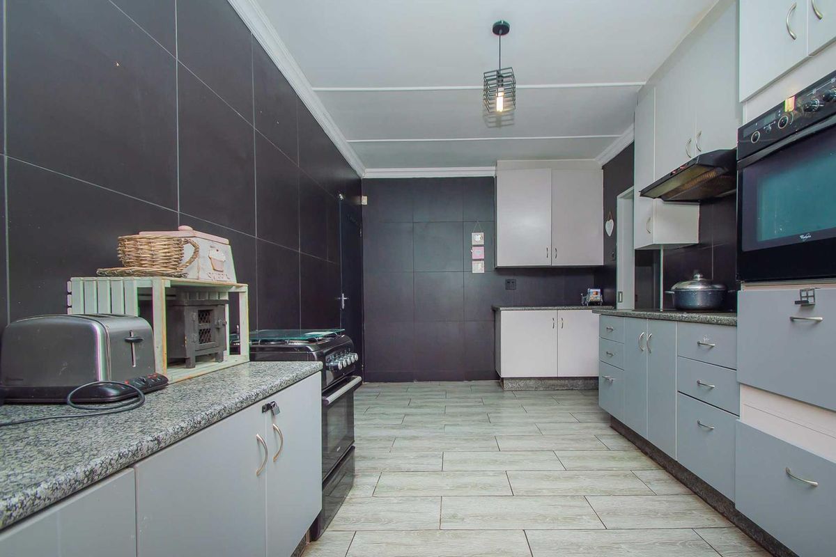 A functional kitchen featuring granite countertops, built-in cabinetry, a built-in oven with extractor fan, and modern tiled flooring and wall finishes.