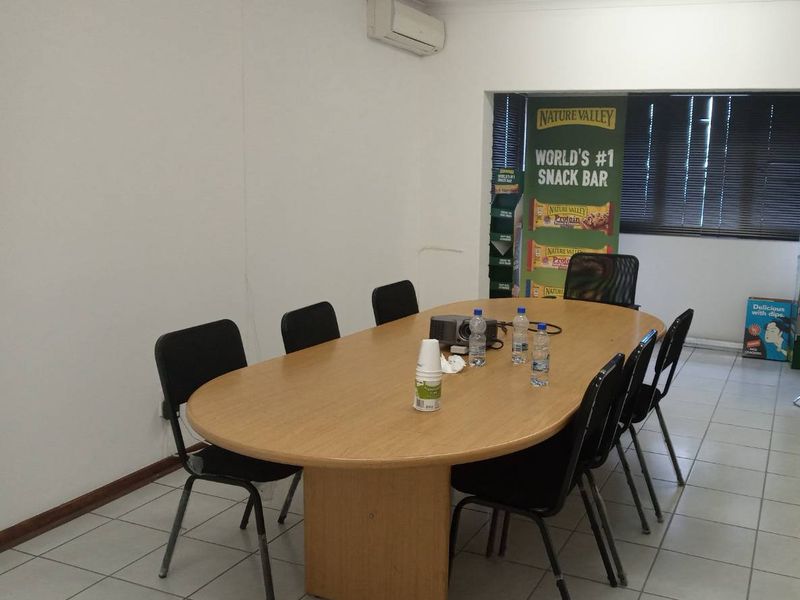 A functional office space featuring tiled flooring, a wall-mounted air conditioning unit, and venetian blinds, suitable for a professional meeting or workspace environment.