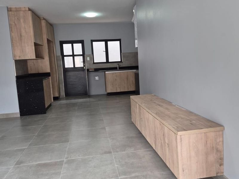 An open-plan living and kitchen area featuring modern wood-finish cabinetry, black granite countertops, and neutral grey tiled flooring throughout.