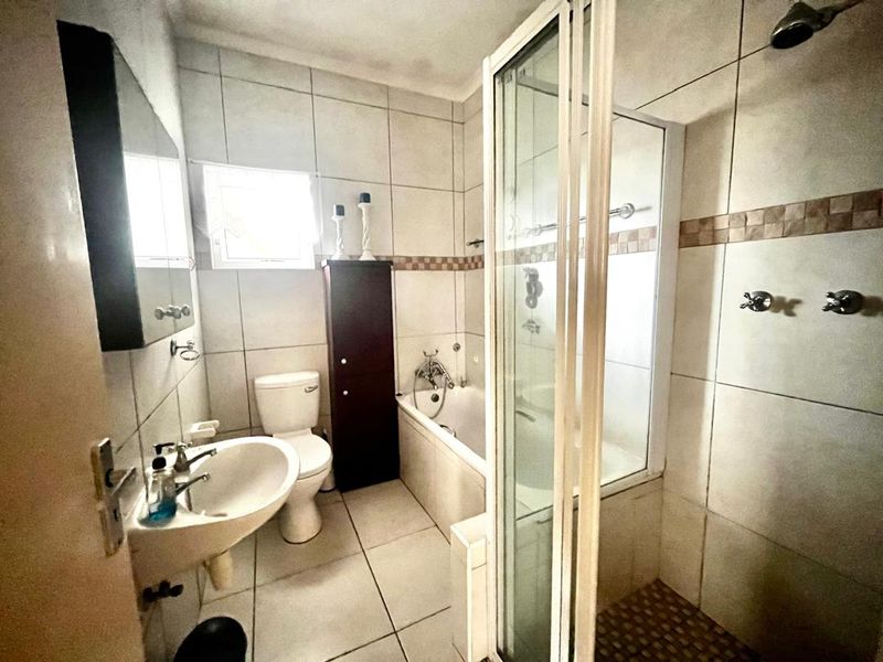 A functional bathroom featuring a separate shower enclosure, bathtub, pedestal basin, and toilet with neutral wall and floor tiling.