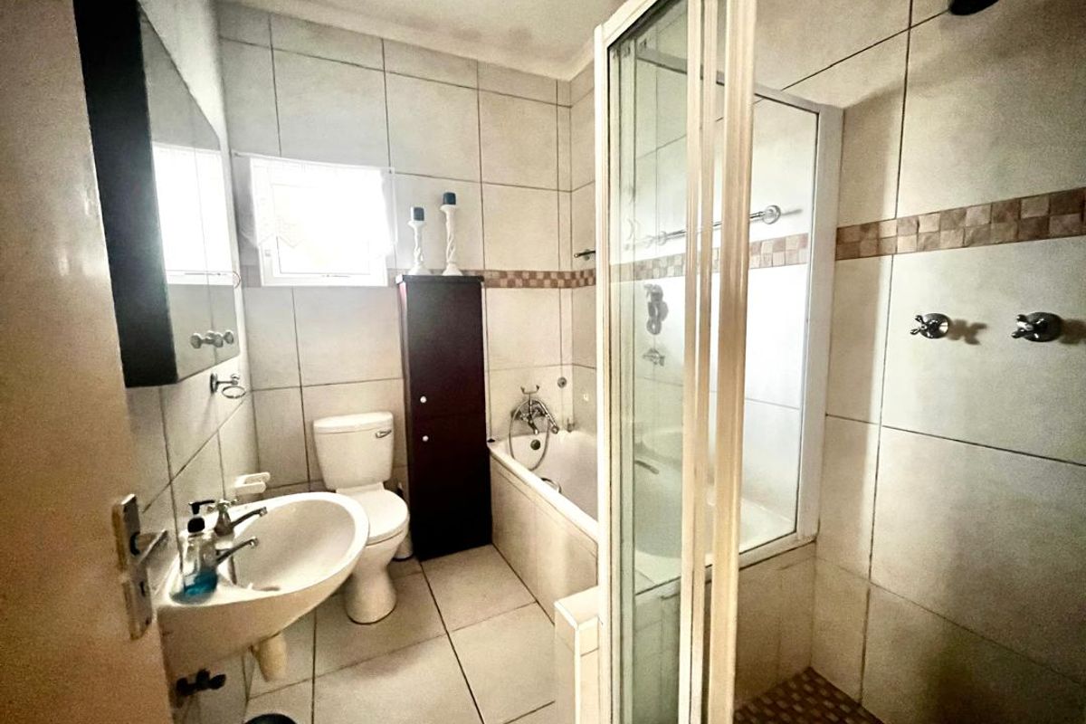 A functional bathroom featuring a separate shower enclosure, bathtub, pedestal basin, and toilet with neutral wall and floor tiling.