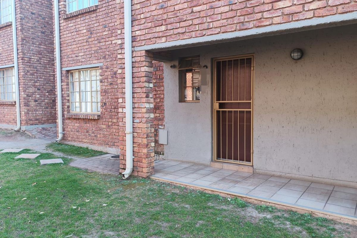 Rear view of the apartment featuring an exposed brick facade, a tiled patio area, and a secure entrance door.