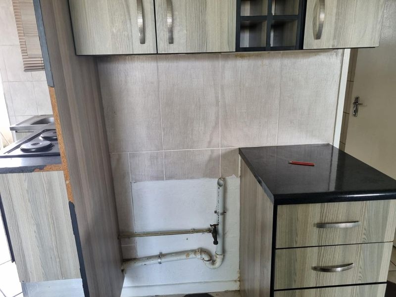 A kitchen area featuring built-in cabinetry and countertops, currently showing exposed plumbing and unfinished wall sections requiring repair or cosmetic updates.