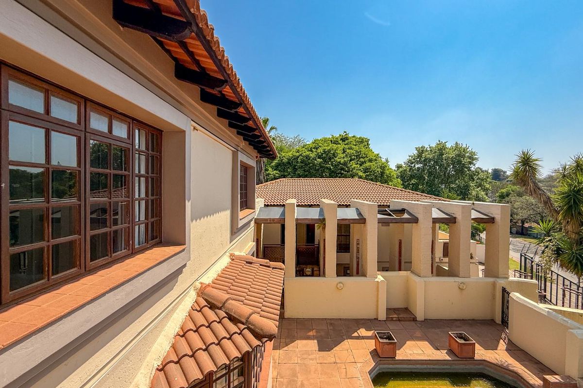 Elevated view of the rear exterior featuring a tiled patio, built-in pool, and architectural columns, showcasing the property's outdoor living space and roof structure.