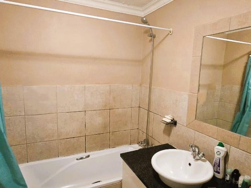 A functional bathroom featuring a built-in bathtub with shower attachment, a vanity basin with granite countertop, and a wall-mounted mirror.