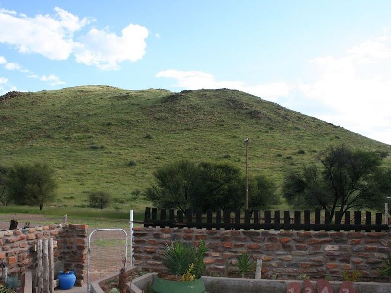 A scenic view of a grassy hill landscape from behind a rustic stone boundary wall and wooden fencing on the farm property.