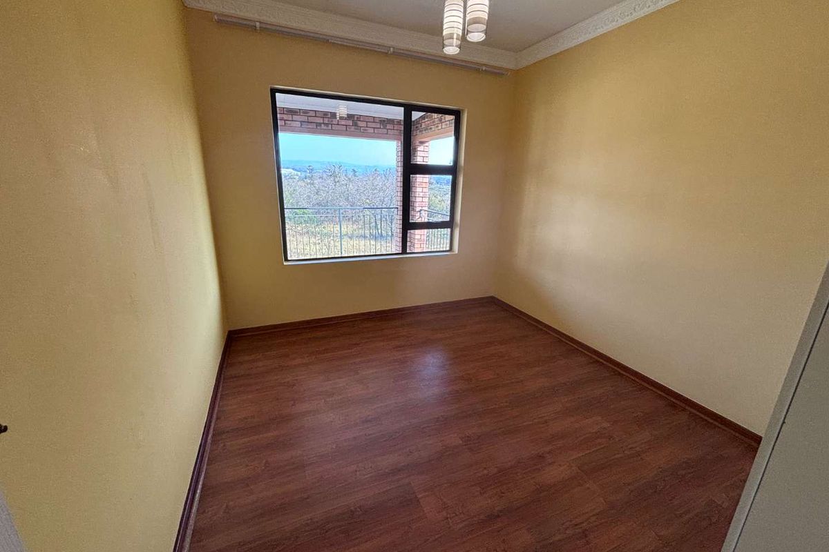 A bright, empty bedroom featuring wood-look laminate flooring, yellow walls, and a large window with views of the surrounding landscape.