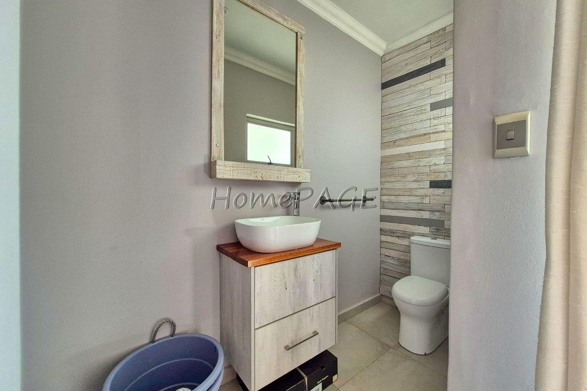 A modern bathroom featuring a vessel sink on a wooden vanity, a wall-mounted mirror, and a toilet with decorative wood-look wall tiling.