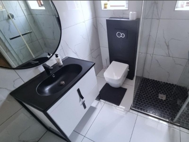 Modern bathroom featuring a wall-mounted toilet, walk-in shower with mosaic floor tiles, and a contemporary vanity unit with a basin.
