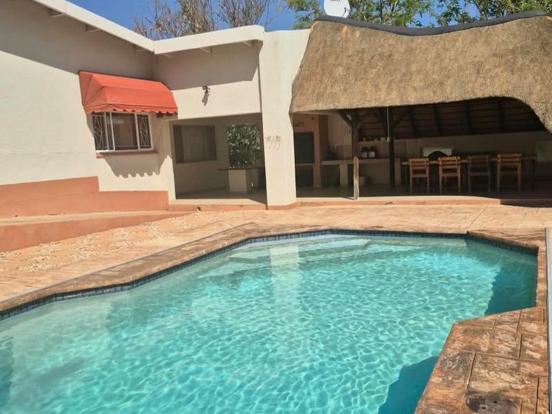 Outdoor pool area featuring a swimming pool, paved deck, and a thatched lapa with a built-in braai, ideal for outdoor entertaining.