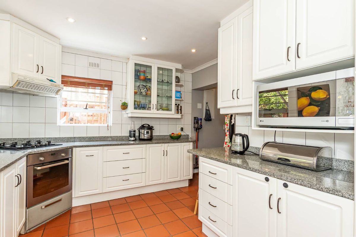 A functional kitchen featuring white cabinetry, granite countertops, a built-in oven, gas hob, and an integrated extractor fan.