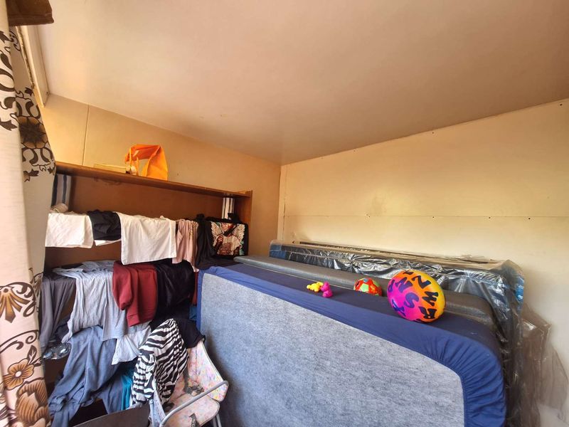 A bedroom space featuring basic wall finishes and built-in shelving, currently used for storage.