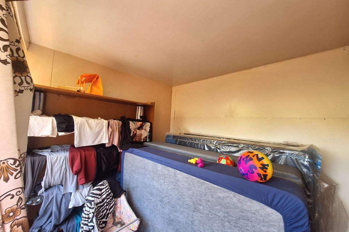 A bedroom space featuring basic wall finishes and built-in shelving, currently used for storage.